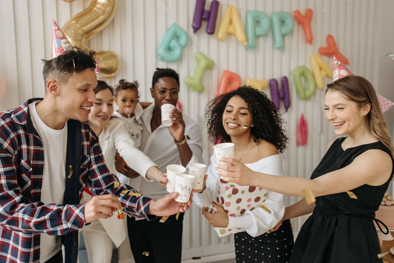 A diverse group of friends celebrating a birthday indoors with party hats and balloons.